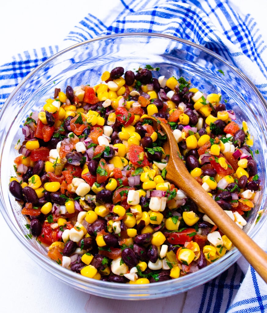 Glass bowl with woodend spoon in black bean and corn salsa.