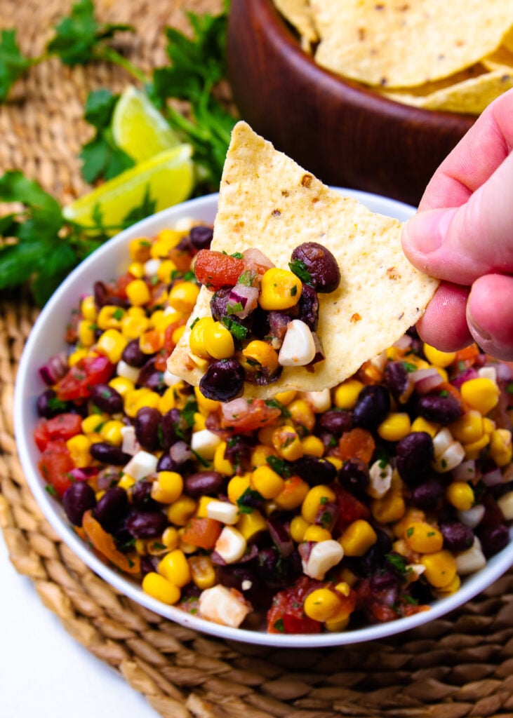 Tortill chip held with hand and black bean and corn salsa