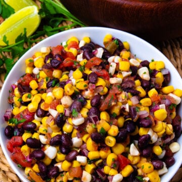 Black Bean and Corn Salsa Recipe served in white bowl with lime, cilantro, tortilla chips, and wooden serving bowl nearby