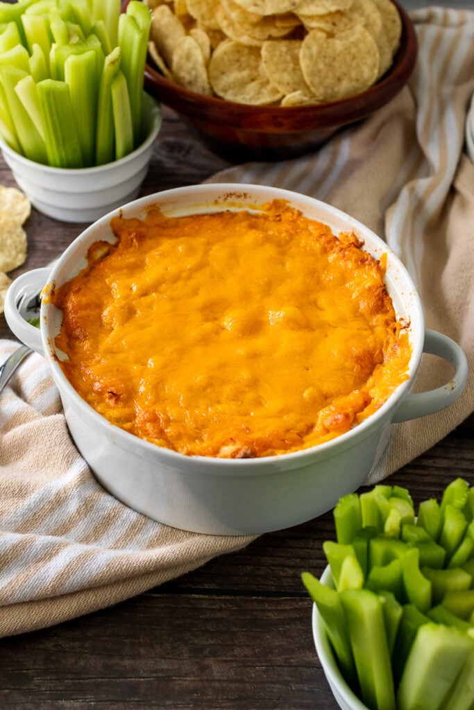 White bowl with baked Buffalo Chicken Dip served with celery sticks and chips.