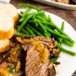 Sliced Pot Roast with onion, green bean and bread on a white plate.