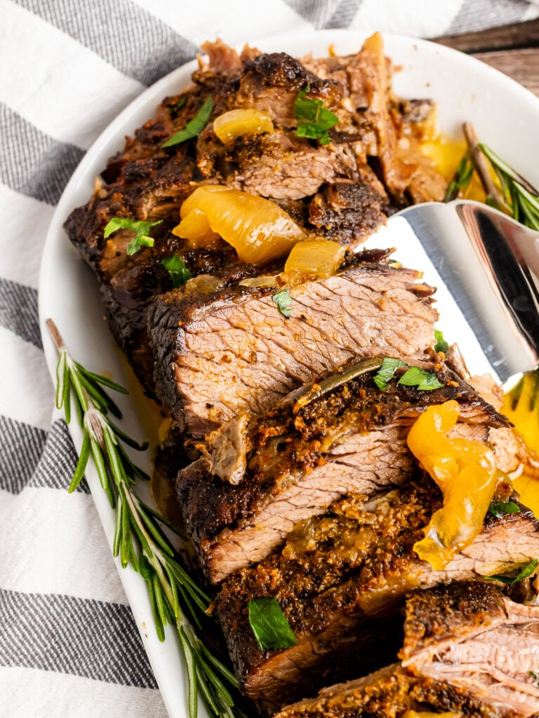 Sliced Slow Cooker Pot Roast with onions and fresh rosemary and a serving spoon.