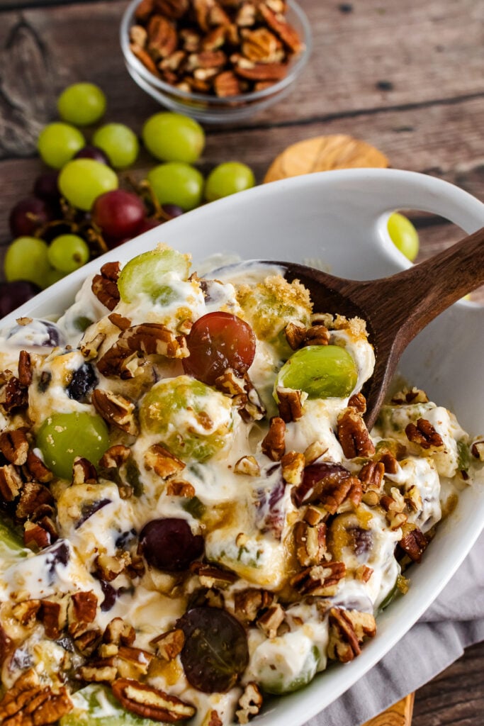 Grape Salad with chopped pecans in a white bowl with wooden spoon.