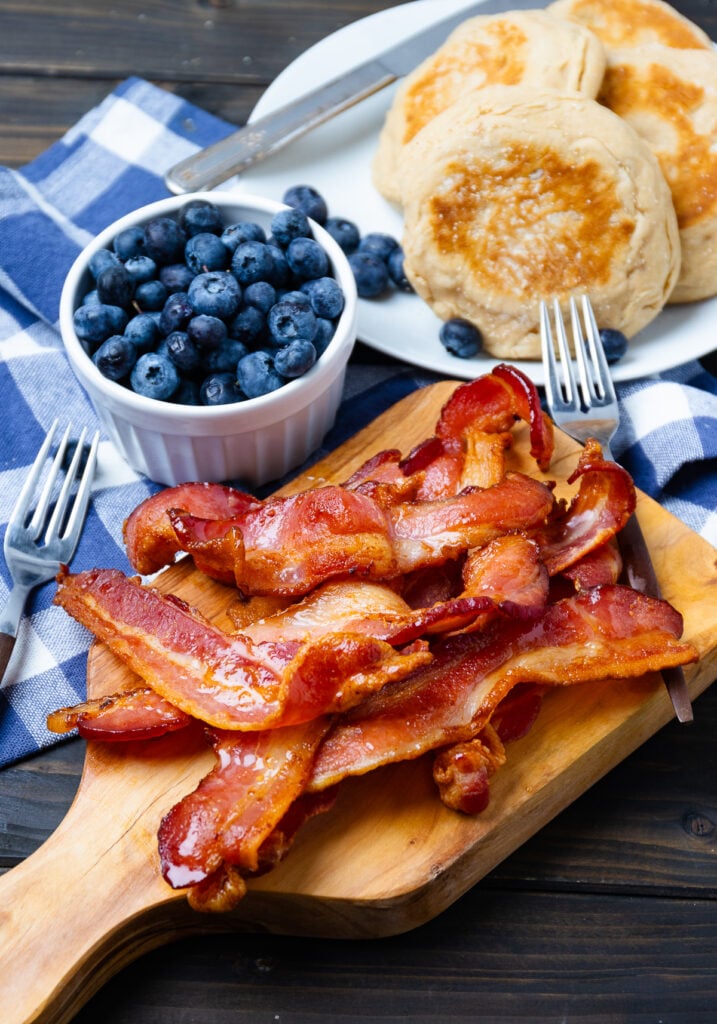 Pieces of cooked bacon with blueberries and english muffins for breakfast.