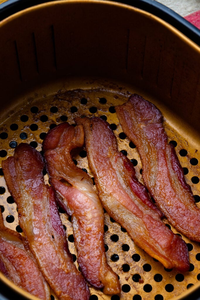 Cooked bacon in the basket of an air fryer.