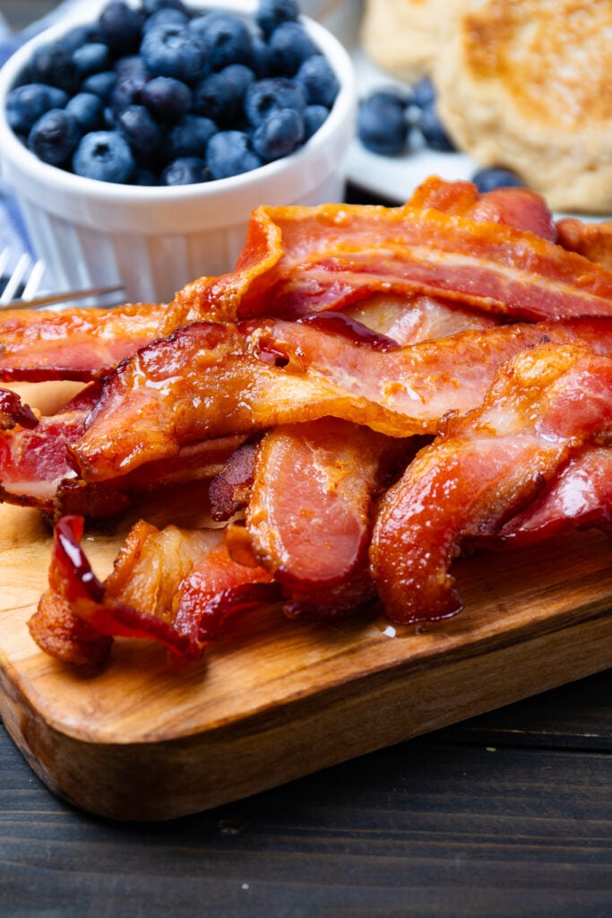 Air fried cooked bacon strips on a woooden cutting board.