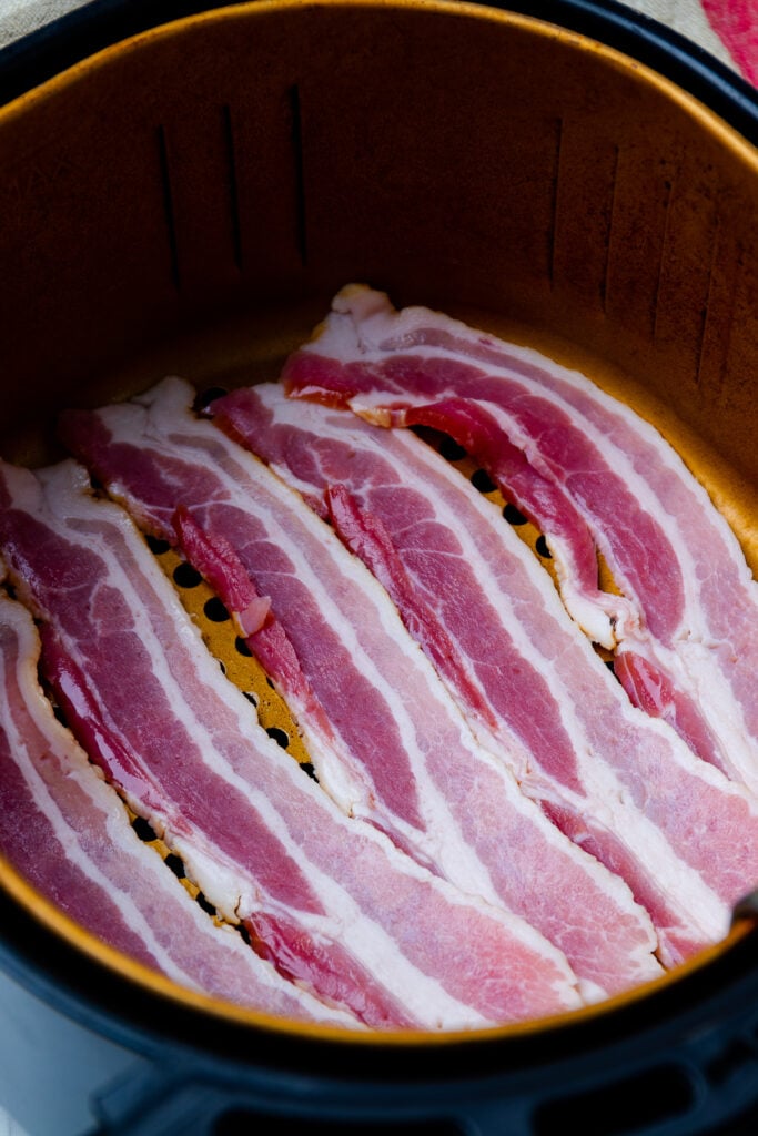 Uncooked bacon in the basket of an air fryer.