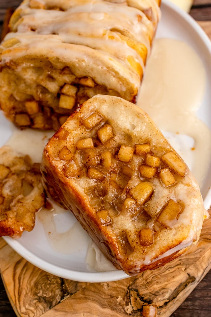 Piece of apple cinnamon pull apart bread on a white plate with apple chunks.