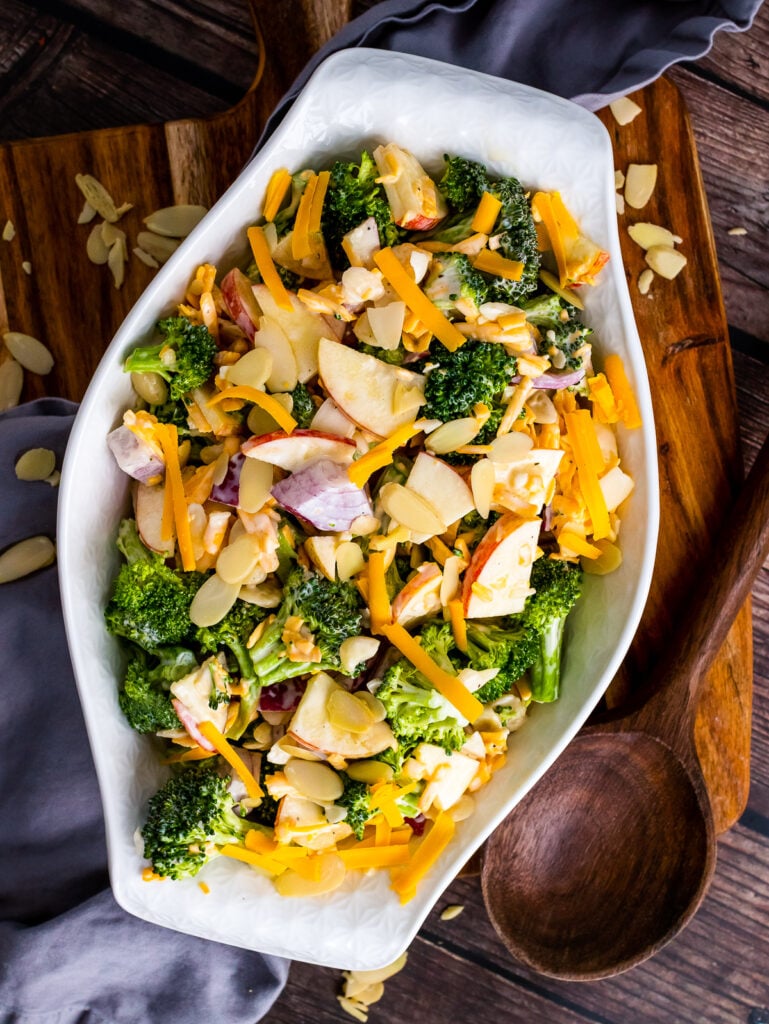 Overhead photo of Broccoli Apple Salad in a white serving bowl with a wooden spoon.