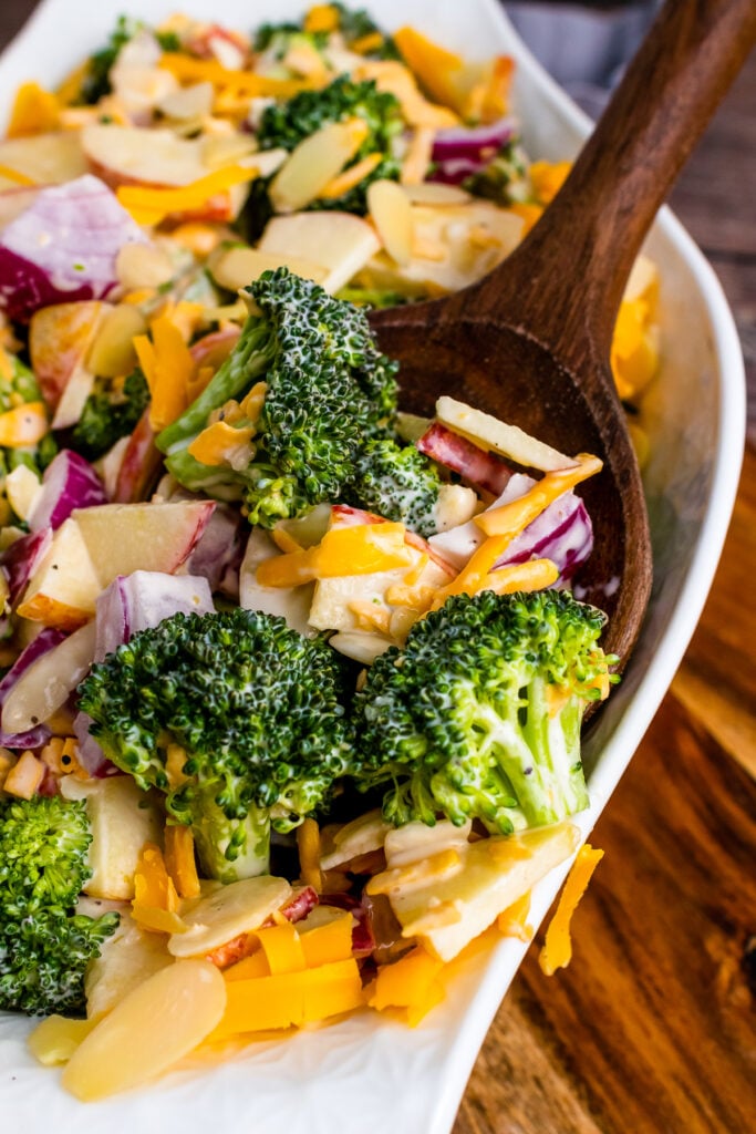 Broccoli Apple Salad with cheese and almonds on a wooden spoon.