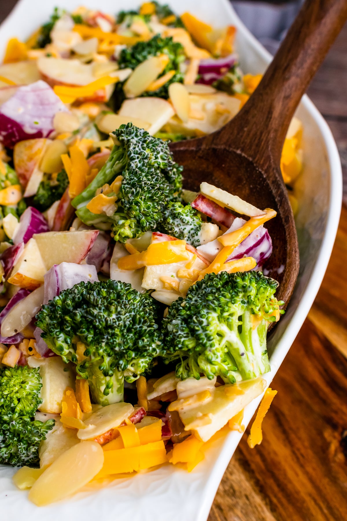 Broccoli Apple Salad with cheese and almonds on a wooden spoon.
