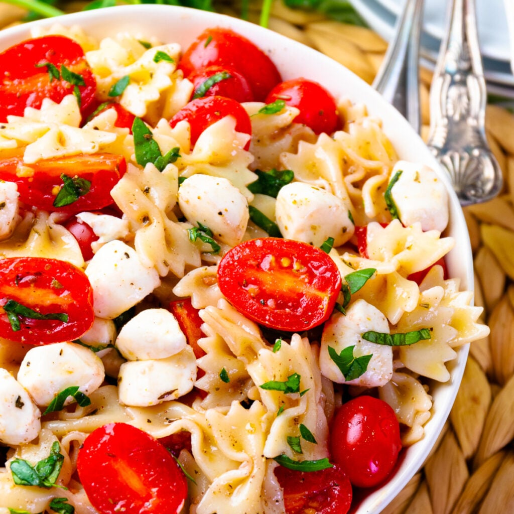 Caprese pasta salad 1200 with bow-tie pasta, fresh mozzarella, red tomatoes, and basil in white bowl with fork
