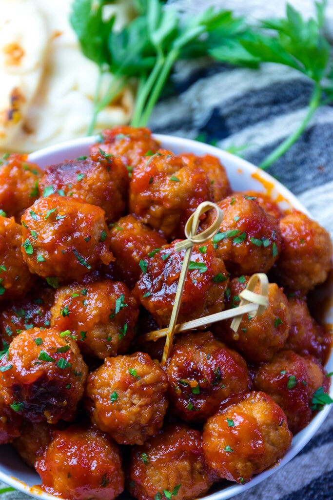 Easy to make, mouthwatering Bourbon Meatballs piled high in a white bowl with two toothpicks for serving.