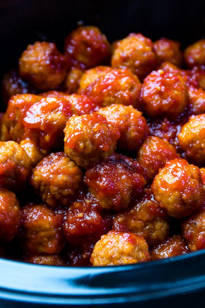 Sweet, tangy Bourbon coated meatballs sit in the base of a black Crock Pot after being slow cooked to perfection.