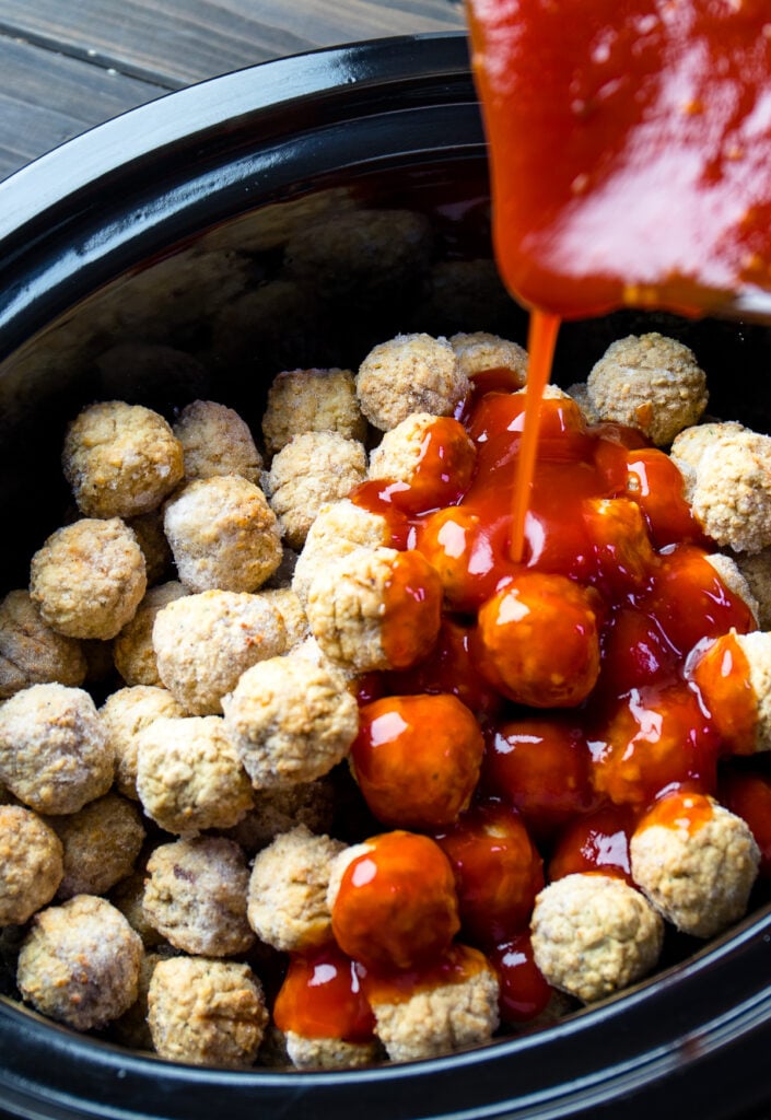 Crock Pot filled with frozen meatballs with a delicious, sweet, and tangy sauce pouring over them.