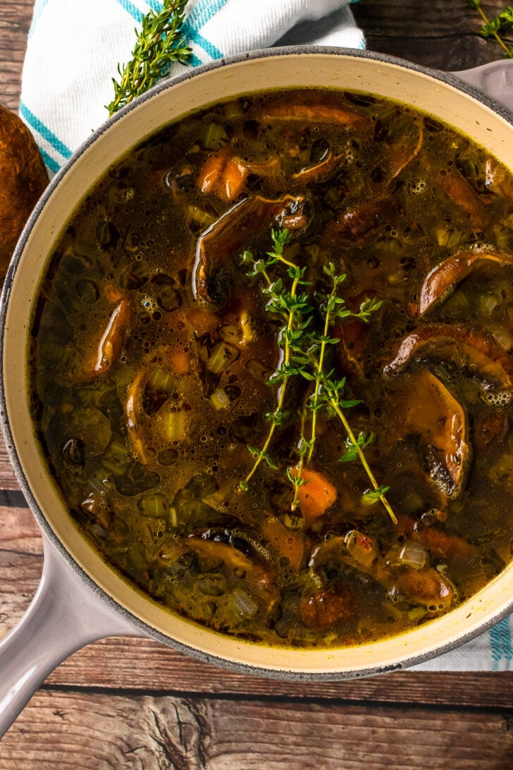 Gray stock pot with mushroom soup and fresh thyme.