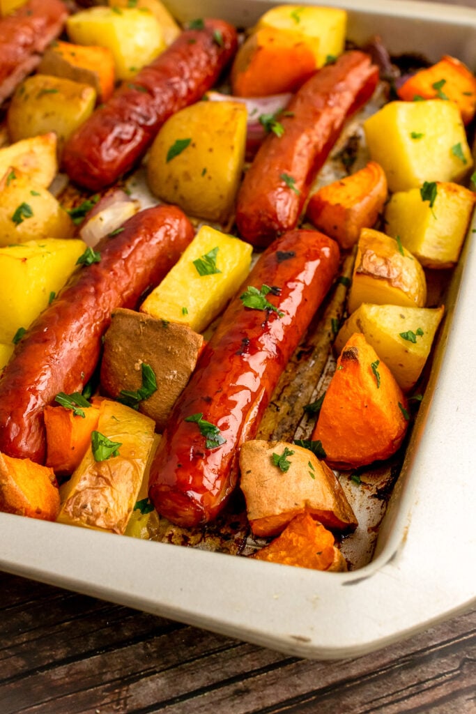 Cooked on a metal sheet pan are Brats with yellow and sweet potatoes.