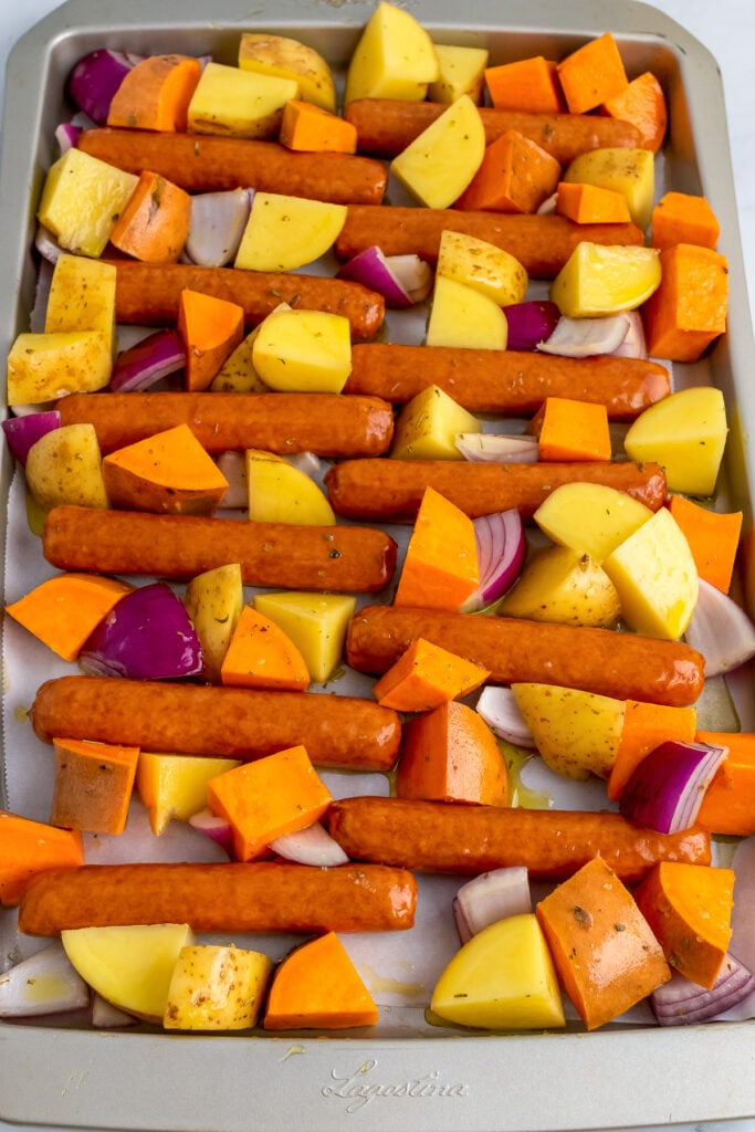 Brats, sweet potatoes, yellow potatoes and red onions on a sheet pan.