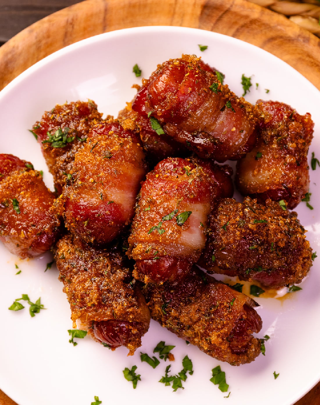 Sweet And Spicy Bacon Wrapped Little Smokies garnished with fresh parsley on a white plate with wooden serving board