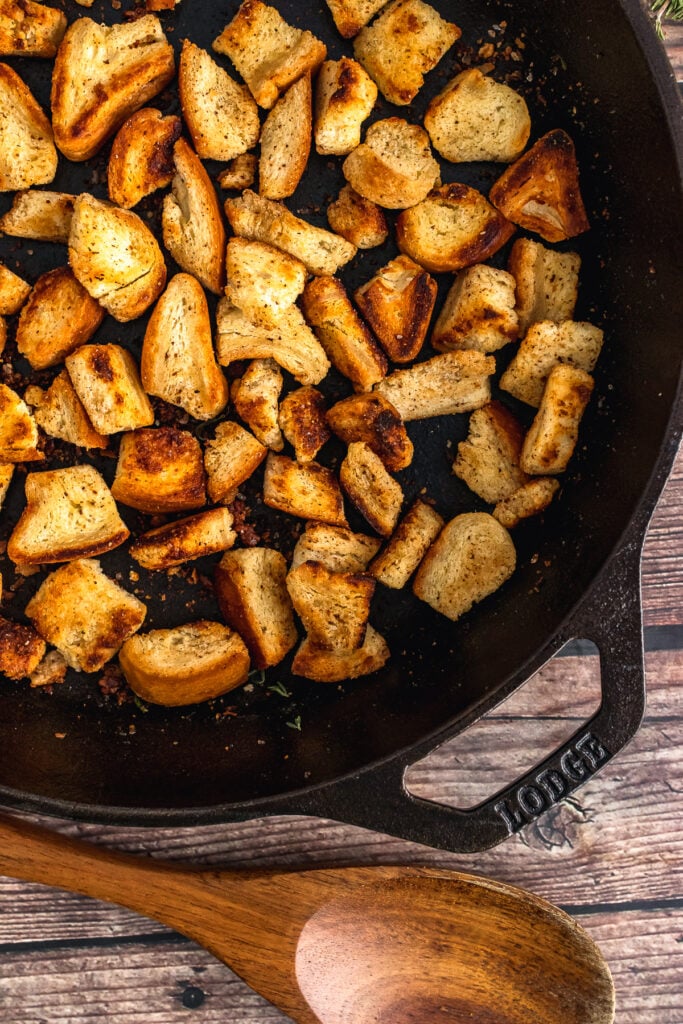 Homemade croutons in a cast iron skillet with a wooden spoon.