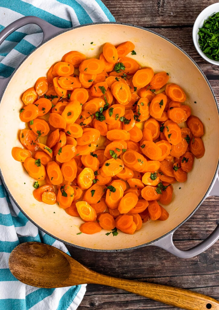 Sautee pan with sliced carrots cooked in honey, butter, and lemon then sprinkled with fresh parsley.