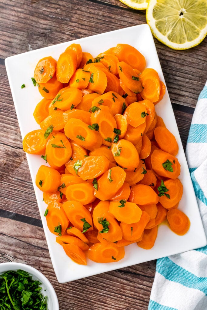 White plate with honey glazed carrots sprinkled with fresh parsley.