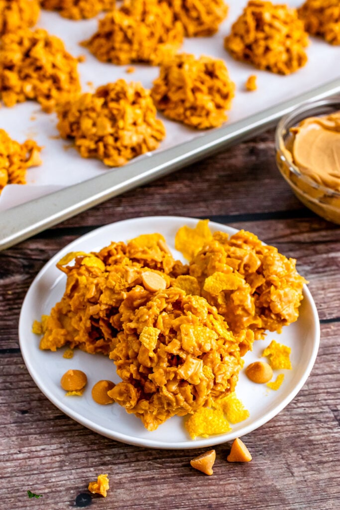 3 butterscotch cookies on a serving plate with more cookies on a baking sheet.