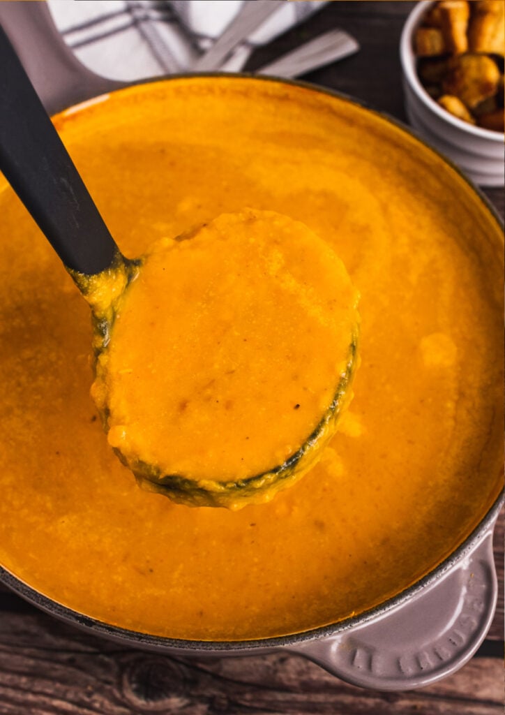 Stock pot full of roasted sweet potato soup served in a ladel.