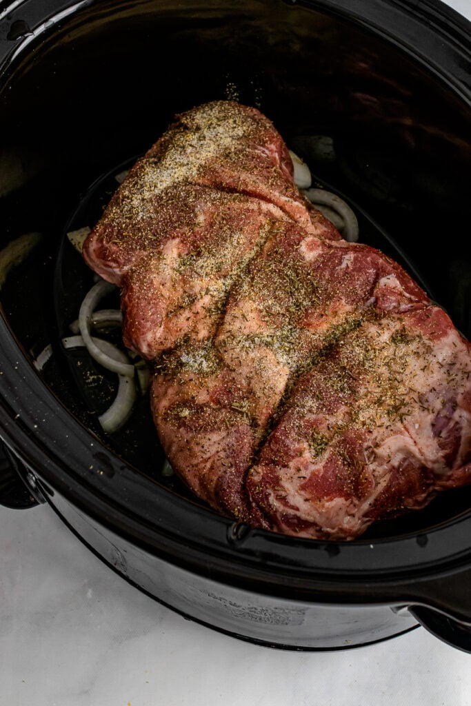 Pork Roast with seasoning and onions in a slow cooker.