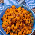 Blue bowl with roasted butternut squash with fresh thyme and a fork for serving.