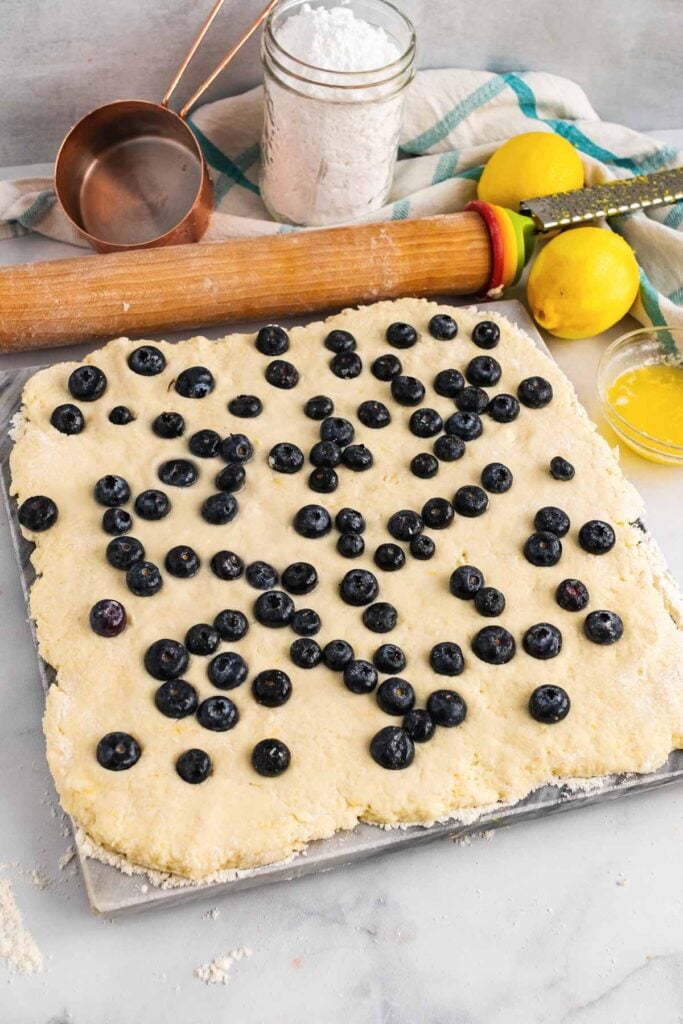 Rolled dough with fresh blueberries on a board to make scones.