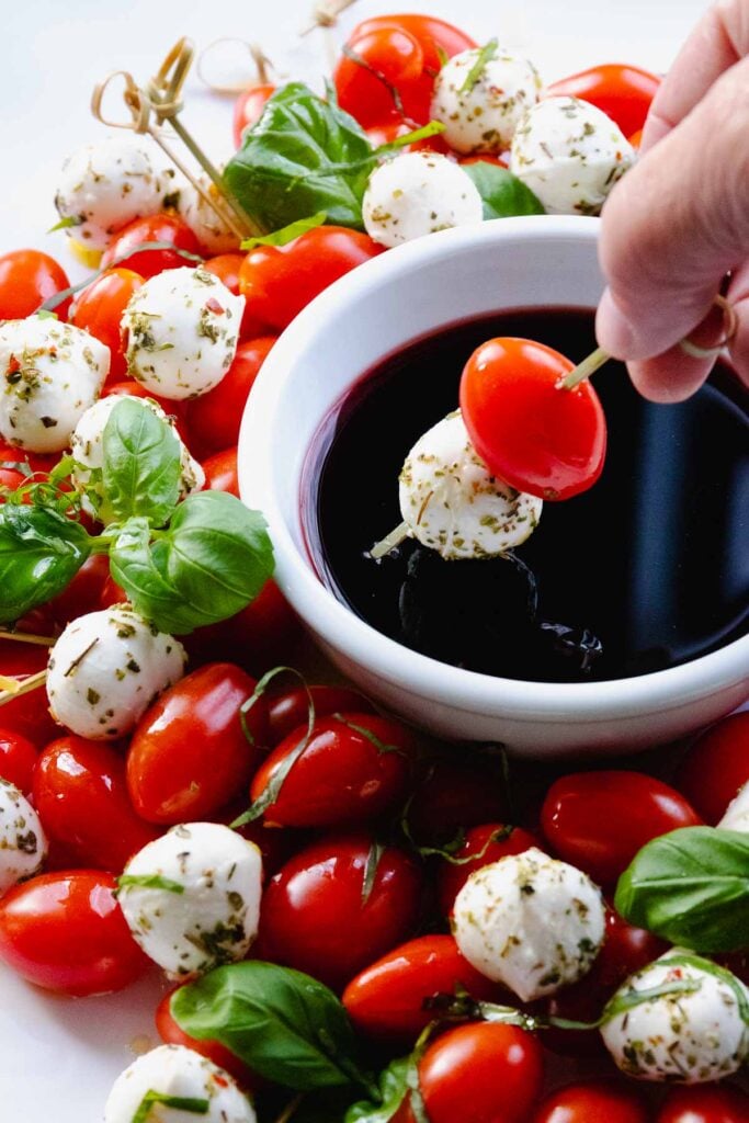 Skewer with grape tomato, and mozzarella being dipped into balsamic reduction.