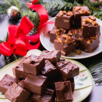 Homemade chocolate fudge pieces on decorative plates with red bow, evergreen garland, and gold ornaments for holiday gift giving