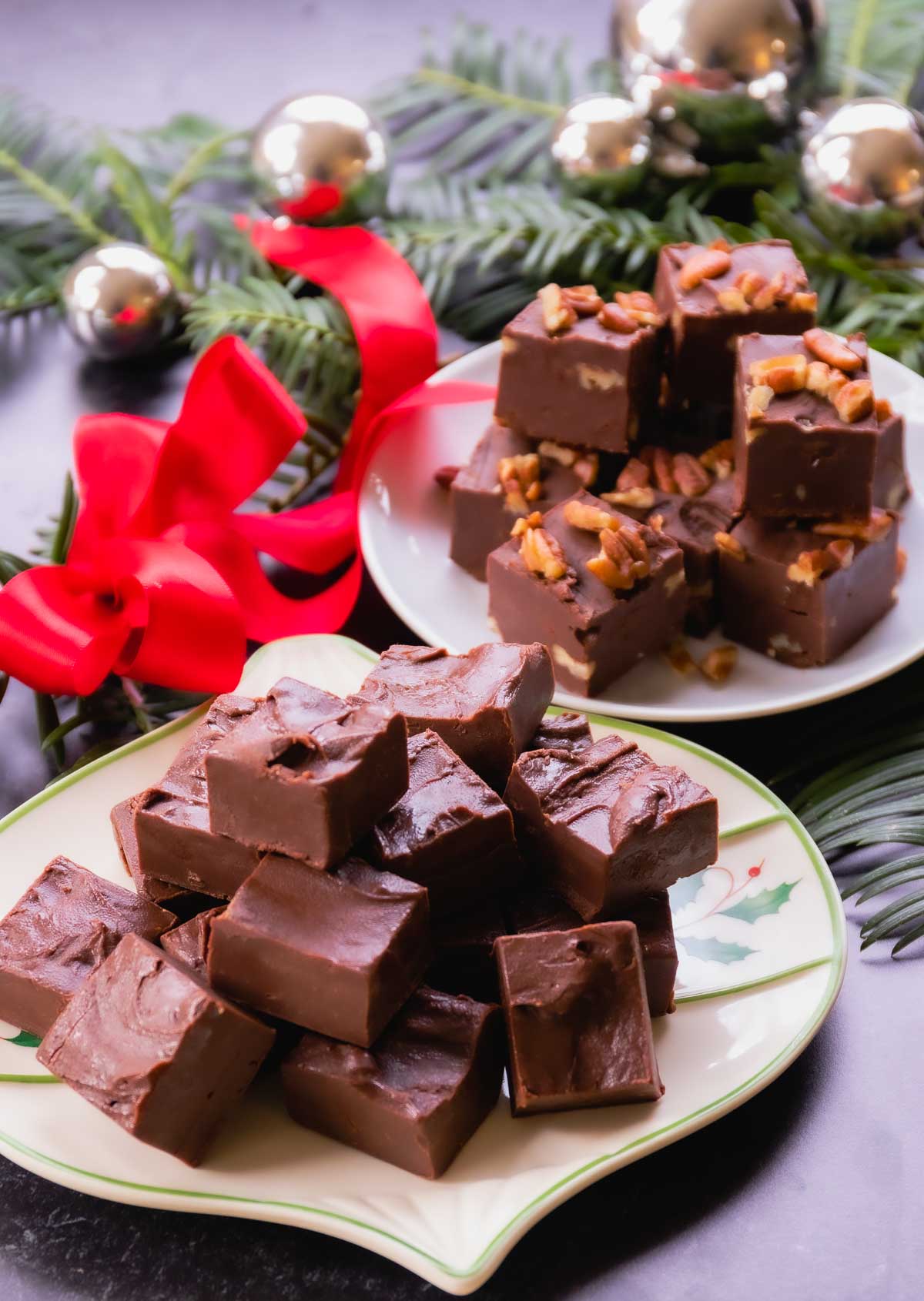 Homemade chocolate fudge pieces on decorative plates with red bow, evergreen garland, and gold ornaments for holiday gift giving