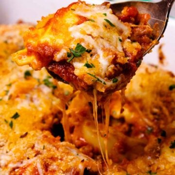 Cheesy Italian Sausage Ravioli Bake on white plate with melted cheese stretching from spoon, garnished with fresh chives
