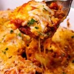 Baked italian ravioli cheese3 with melted mozzarella and red sauce, lifted on a spoon, garnished with fresh chives on a white plate