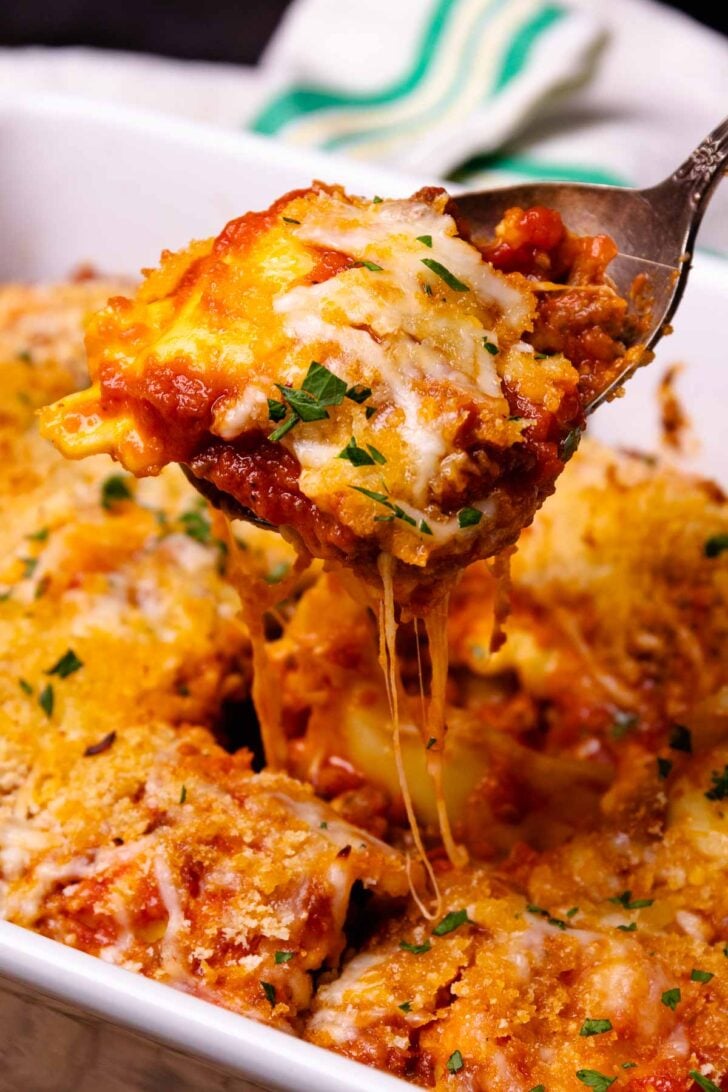 Baked italian ravioli cheese3 with melted mozzarella and red sauce, lifted on a spoon, garnished with fresh chives on a white plate