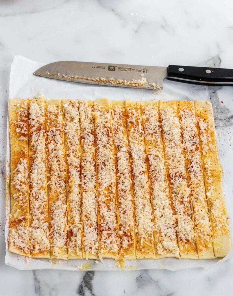 Puffed pastry with parmesan cheese and seasoning cut into strips for cheese straws.