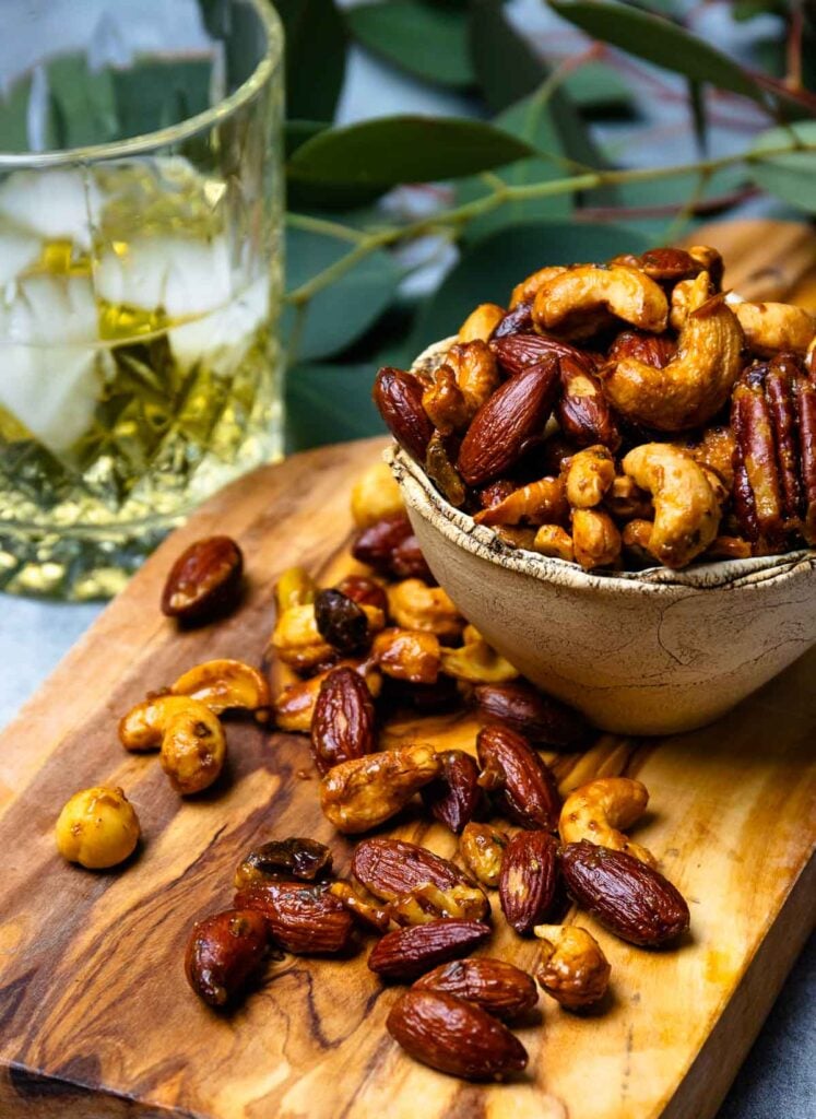 Cocktail drink and Sweet and Spicy Roasted Nuts on a wooden board for cocktail hour.