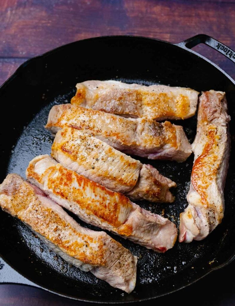 Country style pork ribs in a casted iron skillet that have been seared for cooking.