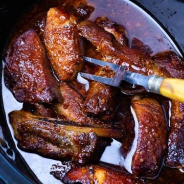 Crock pot full of country style pork ribs being served with a fork.