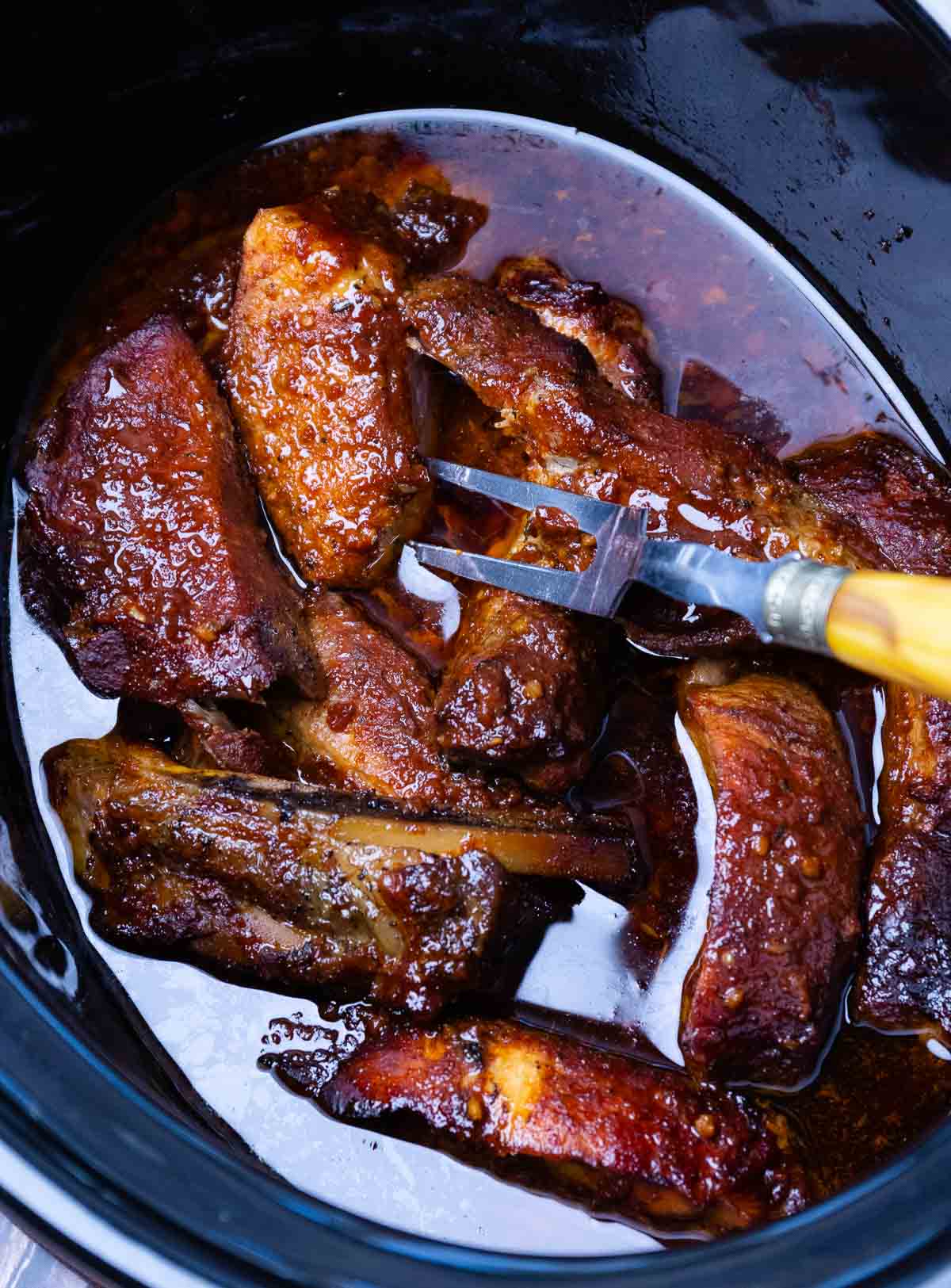 Crock pot full of country style pork ribs being served with a fork.