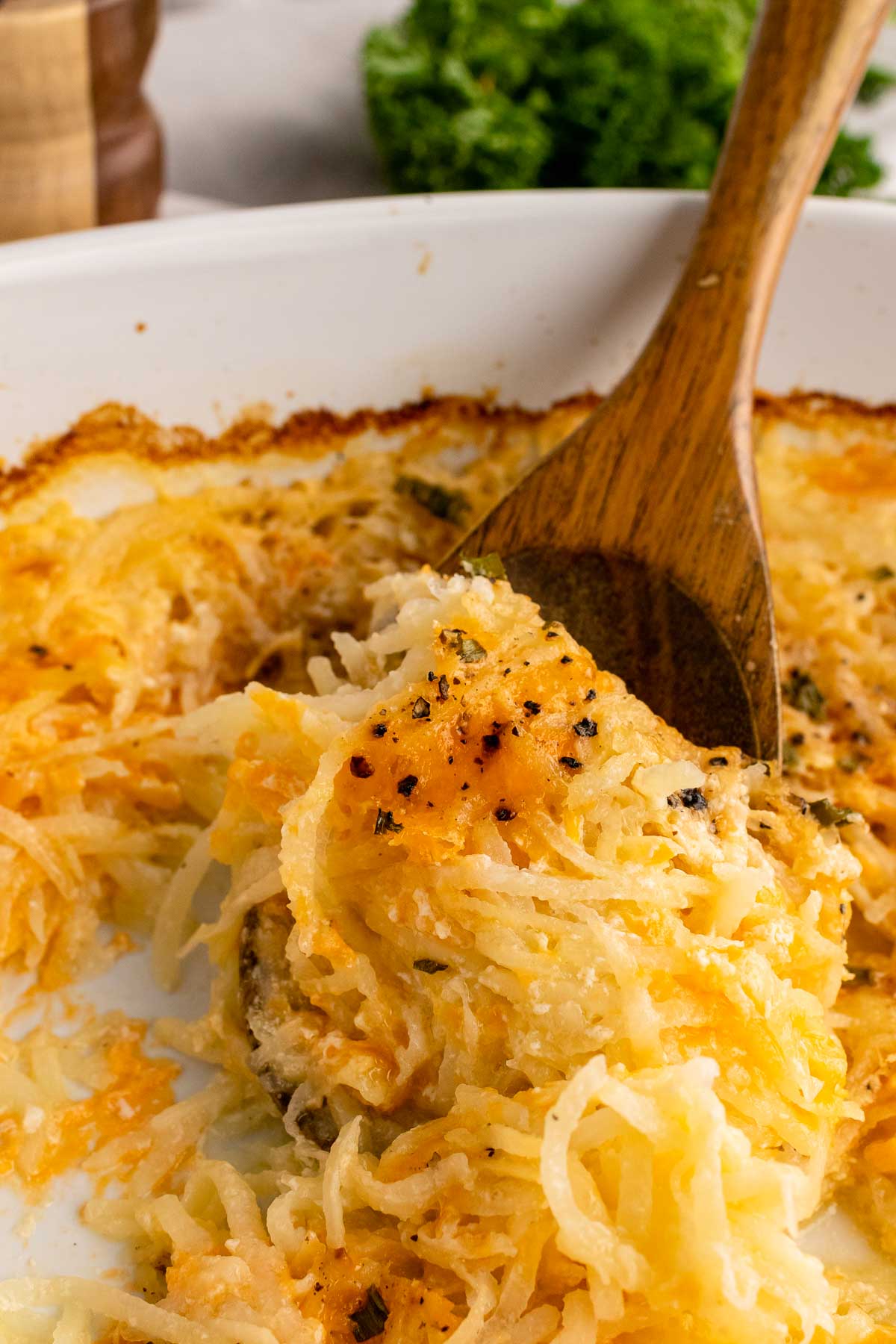 Wooden spoon serving cheesy hash brown casserole.