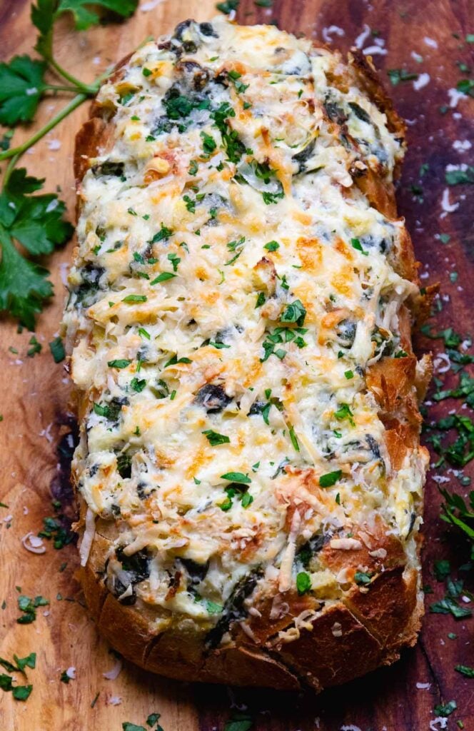 Loaf of baked spinach artichoke bread on a cutting board with parsley.