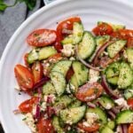 White bowl with cucumbers and tomatoes tossed in Danos homemade spicy dressing in a white bowl and forks for serving.