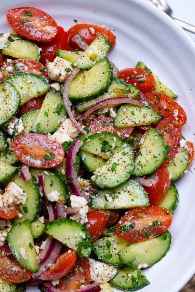 White bowl with cucumbers and tomatoes tossed in Danos homemade spicy dressing.