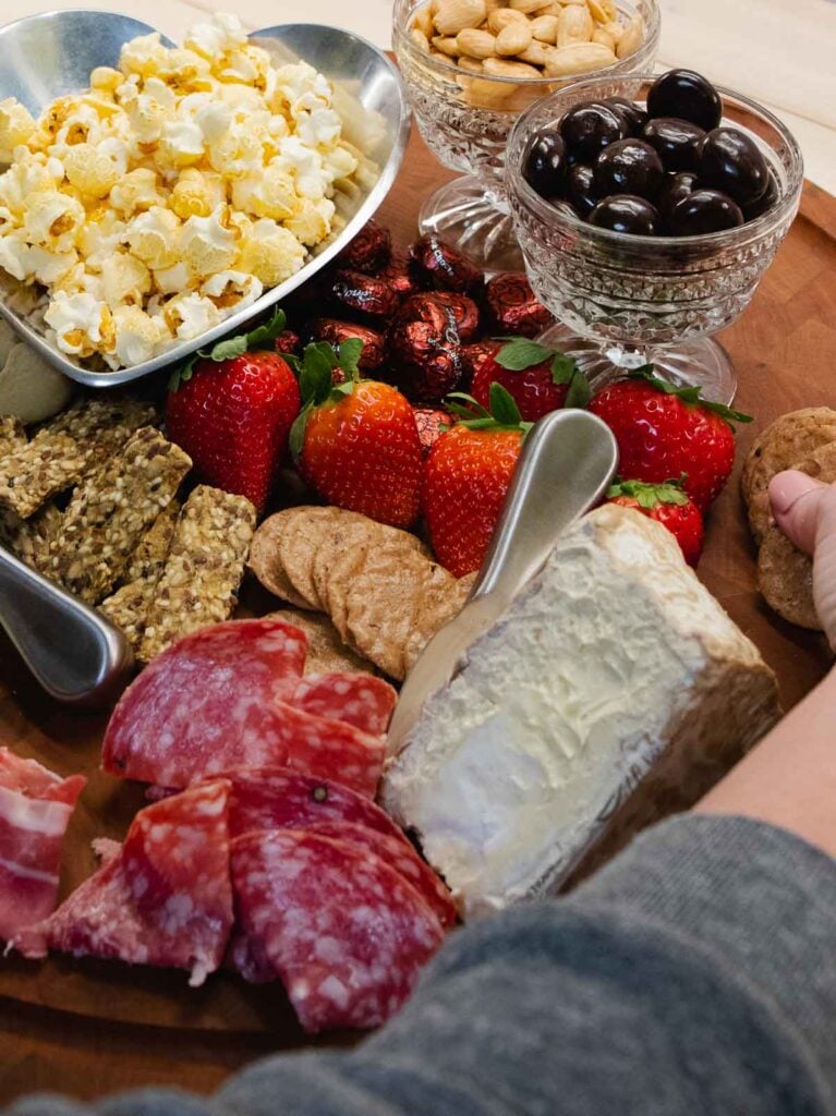 Crackers and cheese with fruit and meat along with chocolates and popcorn.