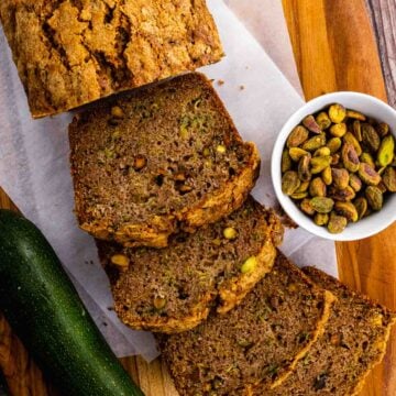 Slices of Zucchini Bread on a cutting board with shelled pistachios.