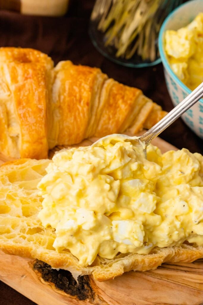 Spoon serving egg salad onto bread.