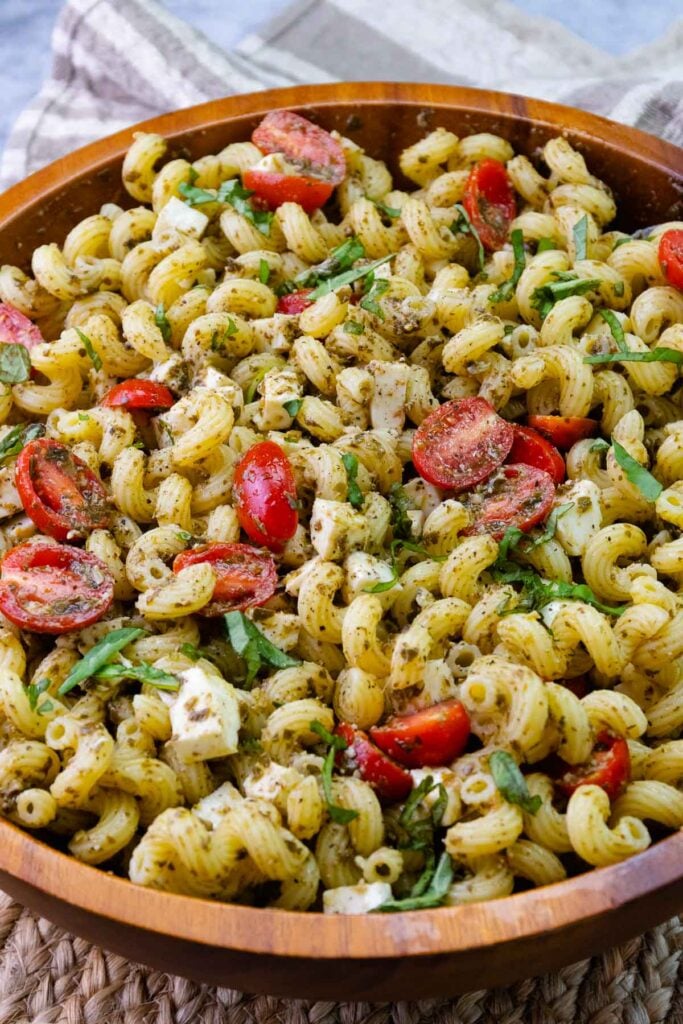 Wooden bowl with pesto pasta salad with tomatoes and cheese.